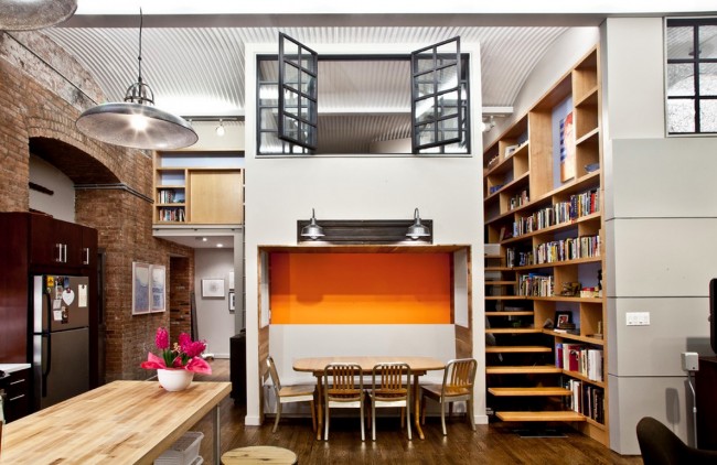 A loft space featuring a kitchen with a dining table and bookshelves.