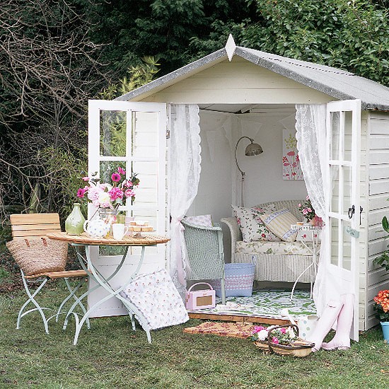 A white garden shed transformed into a cozy diva den with a table and chairs.