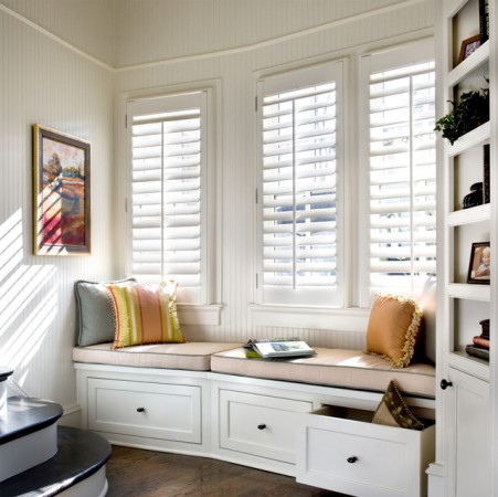 A room with white shutters and window treatments.