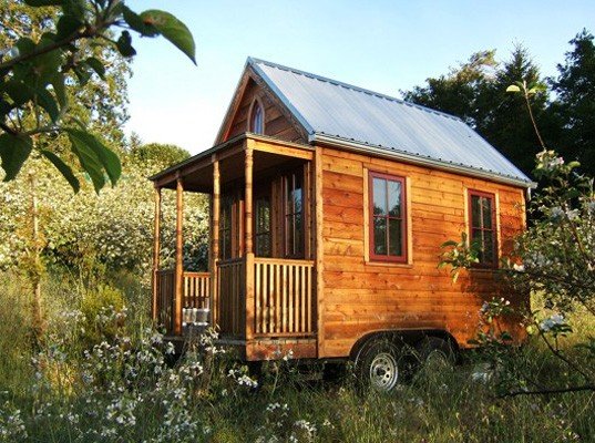 A tiny house resides on a mobile trailer in an open field.