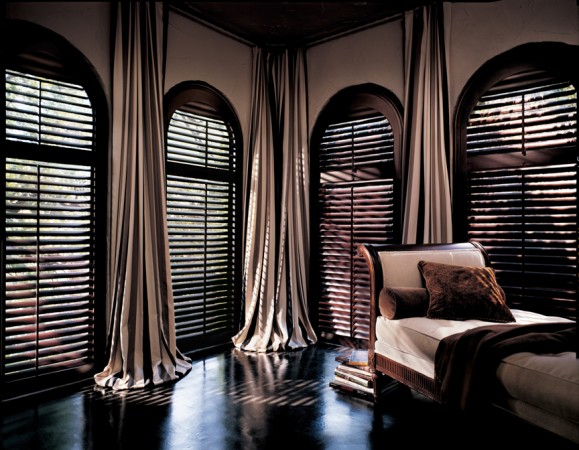 A bedroom with arched window treatments and wooden shutters.
