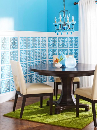 A dining room with blue walls and a green rug featuring latticework.