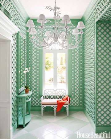 A hallway with green wallpaper and a white bench adorned with latticework.