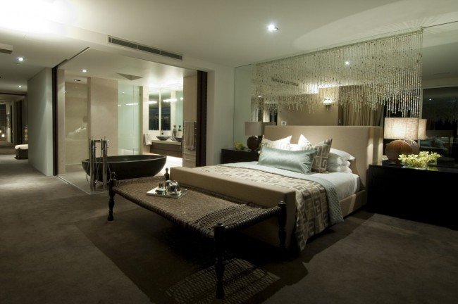 A bedroom with an open bathroom concept featuring a large bed and a large mirror.