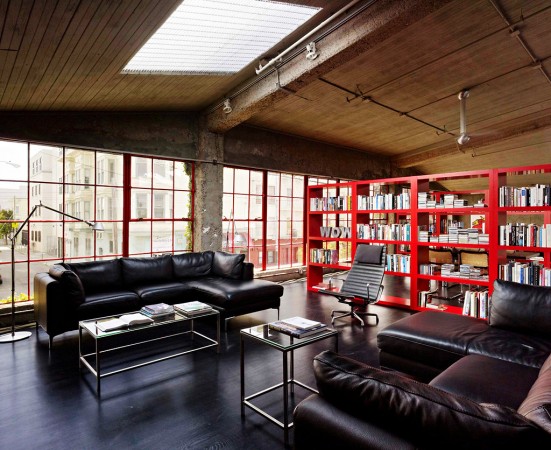A warehouse converted into a home with black leather furniture and a red bookcase.