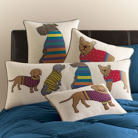 Four decorative pillows on a bed with dogs on them.