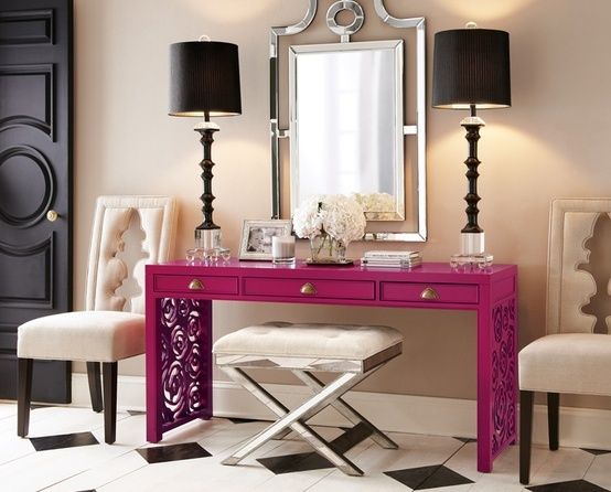 A stylish pink vanity table with a mirror and black chairs.