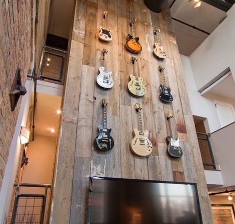 A room with many guitars hanging on the reclaimed wood wall.