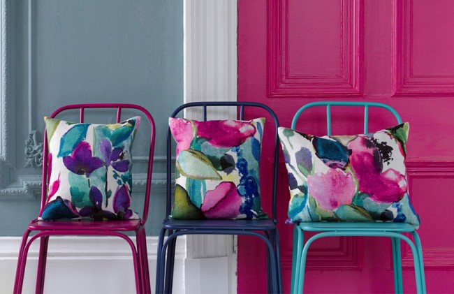 Three chairs with colorful pillows in front of a watercolor blue door.