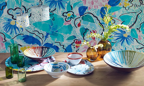 A table with colorful watercolor plates and vases.