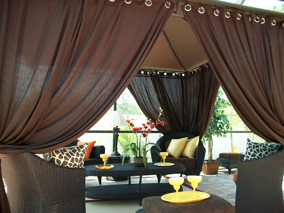 A patio with a canopy and chairs enhanced by curtains.
