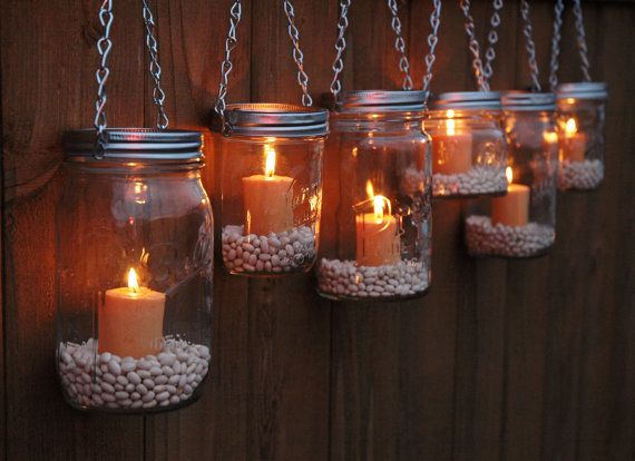 Five mason jars with candles hanging on a wooden fence, decorating.
