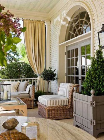 A porch with wicker furniture and a table adorned with curtains.