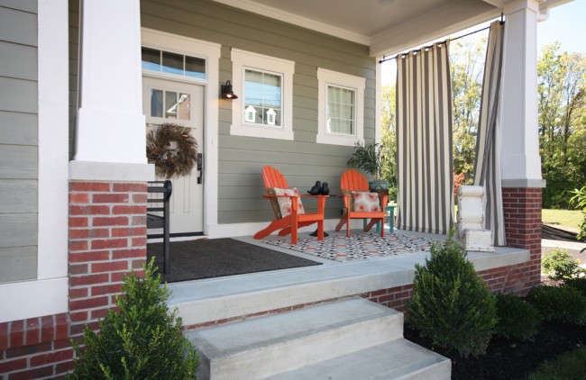 The front porch of a home has orange chairs on it, how curtains perk up your outdoor space.