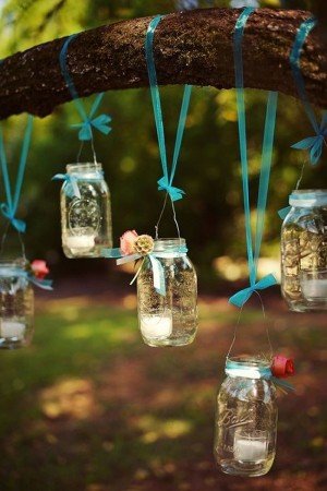 Mason jar lanterns hanging from a tree, decorating with candles.