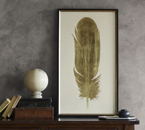 A gold feather displayed on a decorative table alongside a vase, adding an elegant touch to your nest.