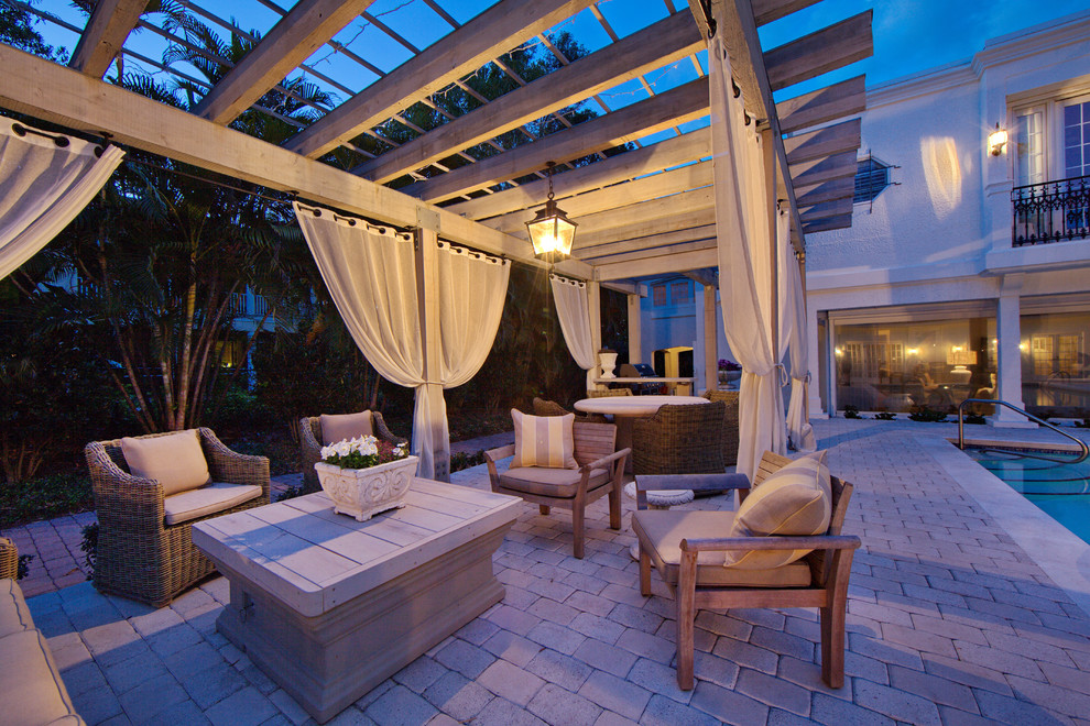 A patio with wicker furniture, curtains and a pool.
