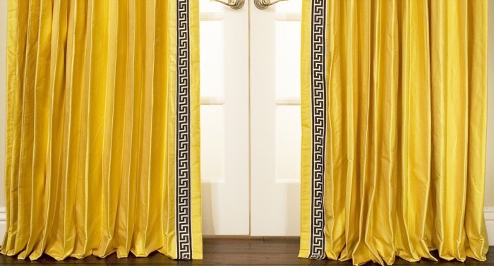 A pair of yellow curtains with a Greek Key design trim.