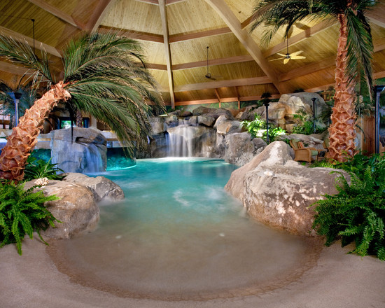 An inspiring indoor swimming pool featuring a waterfall and palm trees.