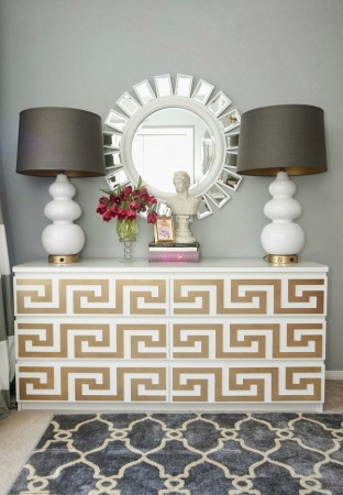 A gold and white dresser with a Greek Key design mirror and two lamps.