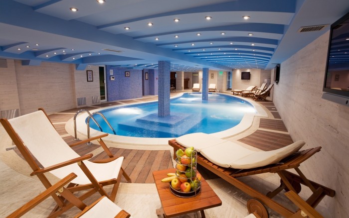 An inspiring indoor swimming pool with lounge chairs and a blue ceiling.