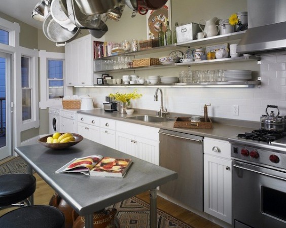A kitchen with stainless steel counter tops and stainless steel appliances featuring open shelving.