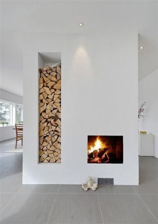 A white room with a cozy fireplace filled with stacked wood.