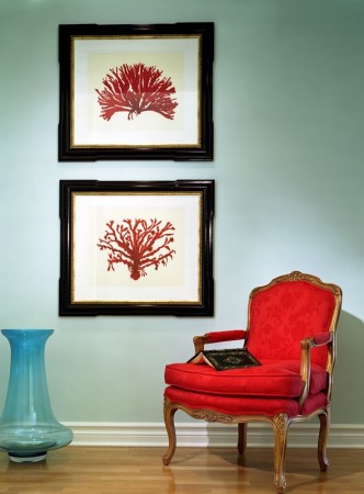 A red chair and two framed pictures on a wall with ocean accents.