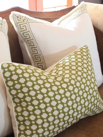 Green and white Greek Key Design pillows on a brown couch.