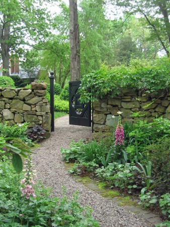 A rock wall surrounds a gate for a lovely garden entrance