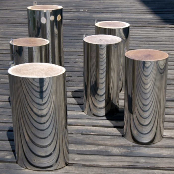 A group of stainless steel stools on a wooden deck, surrounded by tree trunks.