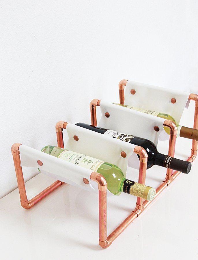 A copper pipe wine rack with three bottles.