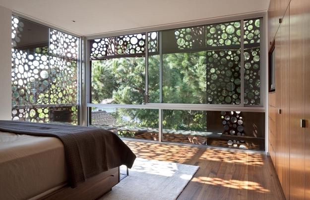 A trendy bedroom with a large window overlooking a wooded area featuring a perforated design.
