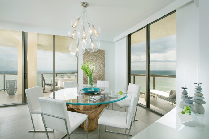 A elegantly designed dining room with a glass table and chairs showcasing a stunning view of the ocean.