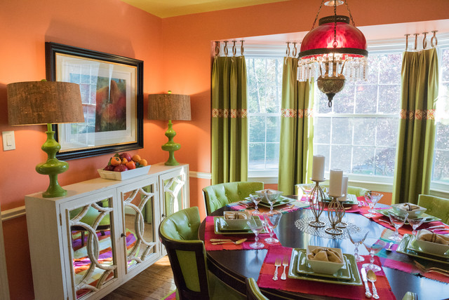 A dining room with bold orange walls and wonderful green chairs.