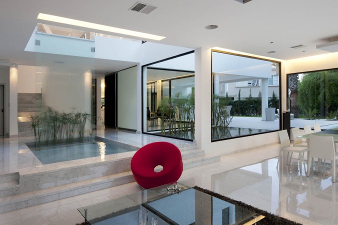 A modern living room with glass walls and a red chair incorporating marble accents.