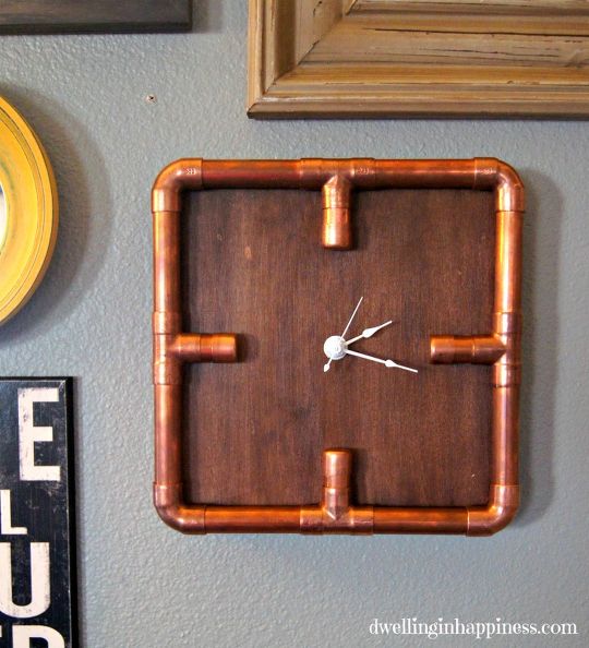 A copper pipe clock is hanging on a wall.