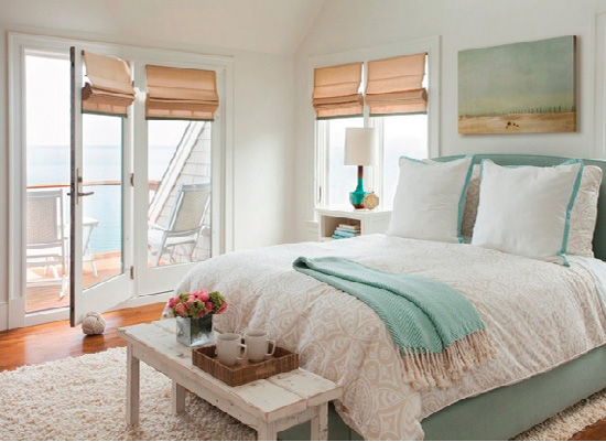An elegant bedroom with an understated coastal design featuring a white bed and a view of the ocean.