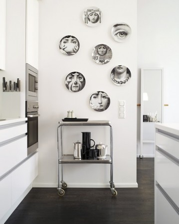 A white kitchen with Piero Fornasetti plates on the wall.