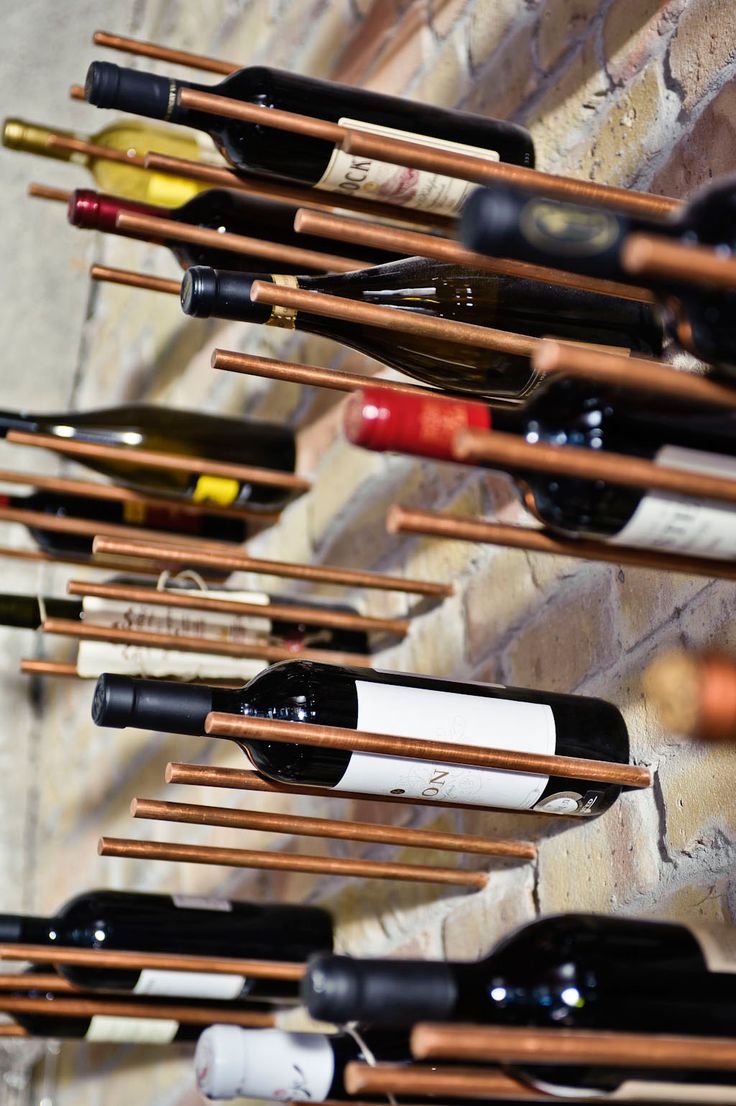 A copper pipe wine rack with many bottles hanging on it.