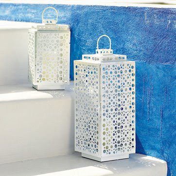 Two white lanterns with a trendy perforated design on steps next to a blue wall.
