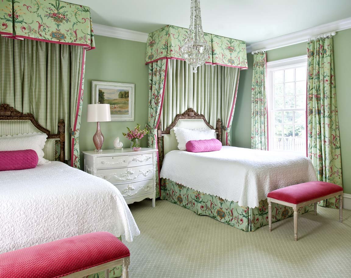 A green and pink bedroom with twin beds and a chandelier.