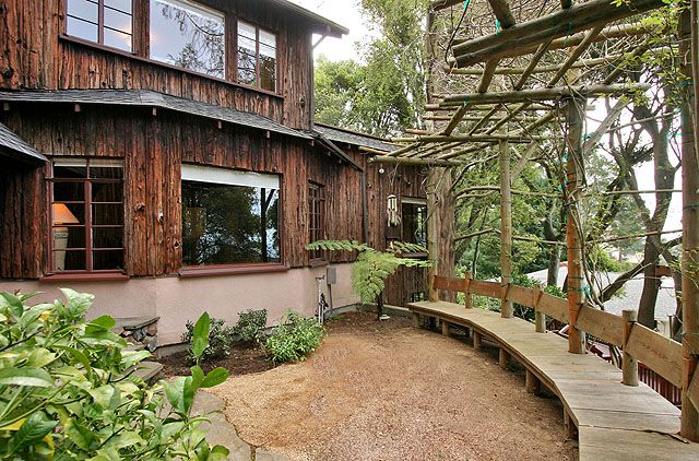 A wooden walkway leads to a charming wooden house in a wonderful backyard retreat.