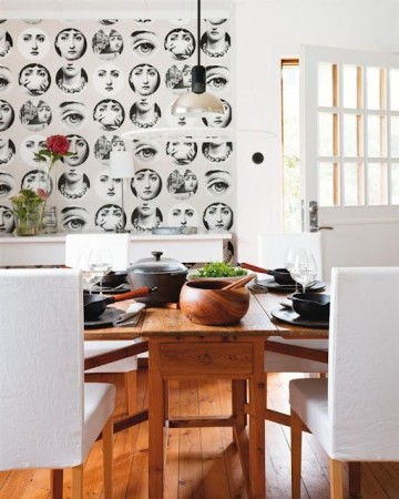 A dining room with a Piero Fornasetti-inspired black and white wallpaper.