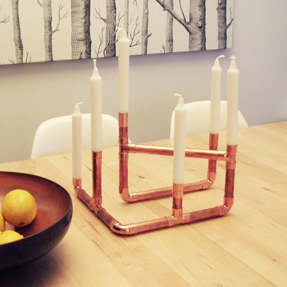 A copper pipe candle holder sits on a wooden table.
