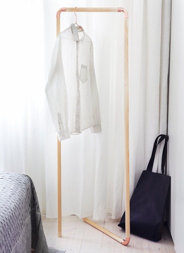A white shirt hangs on a wooden rack in a copper pipe bedroom.