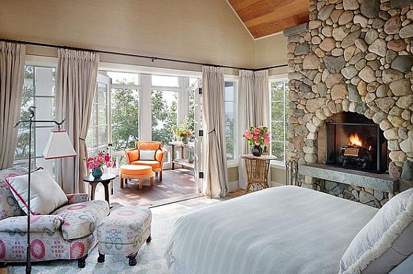 A lakefront bedroom showcasing stone walls and a cozy fireplace.