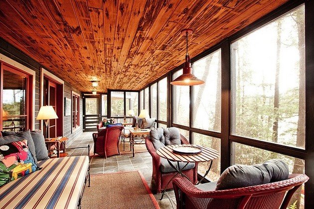 A screened porch with wicker furniture and a view of the woods in a lake home.