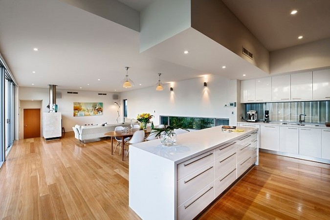 A modern kitchen with wooden floors and white walls, featuring an open floor plan.