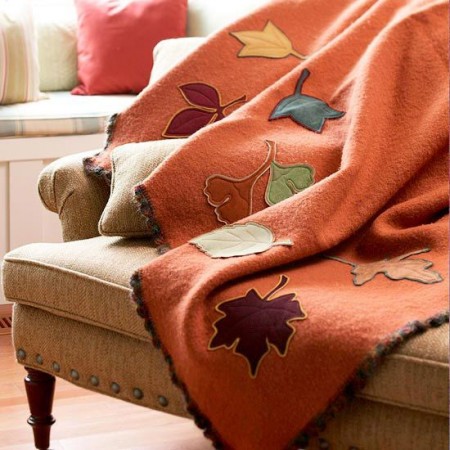 A blanket with leaves on it is sitting on a couch, perfect for fall.